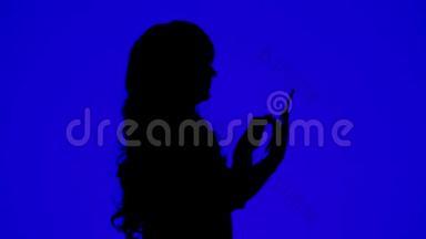 一个身材苗条、卷发的女人在蓝色背景的平板电脑上用信使传达信息的剪影